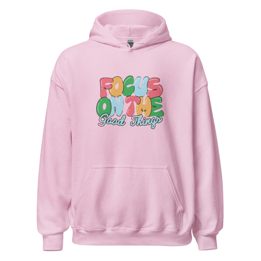 Pink hooded sweatshirt with a central graphic reading "Focus On The Good Things" in multi-color retro bubble letters with a light blue outline|IslandWear Fashion
