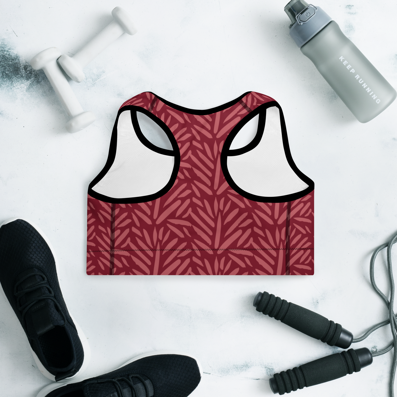 Maroon sports bra with a subtle abstract red leaf/brushstroke pattern, displayed on a gym flat lay with dumbbells and sneakers | IslandWear Fashion 