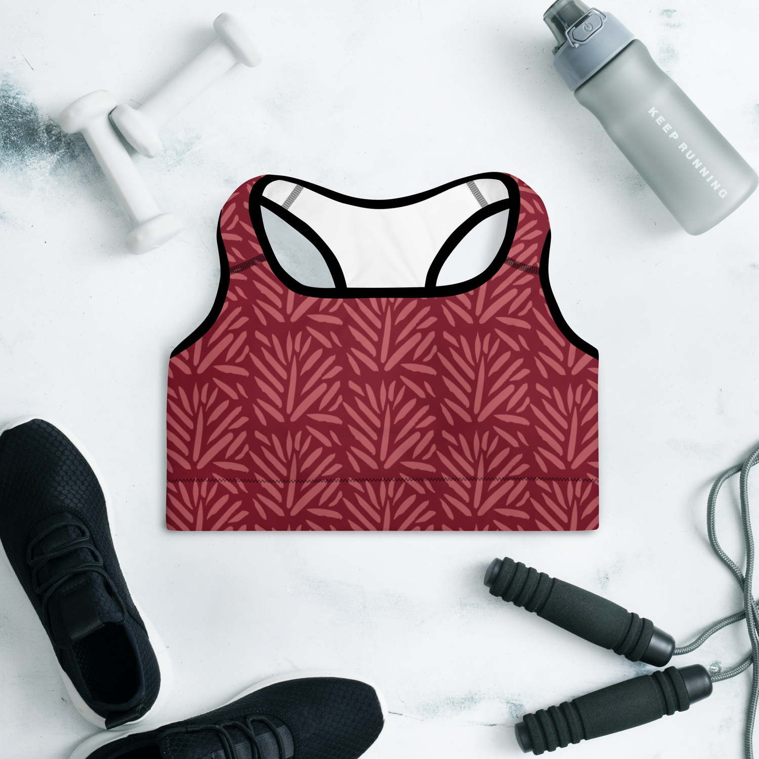 Maroon sports bra with a subtle abstract red leaf/brushstroke pattern, displayed on a gym flat lay with dumbbells and sneakers | IslandWear Fashion 
