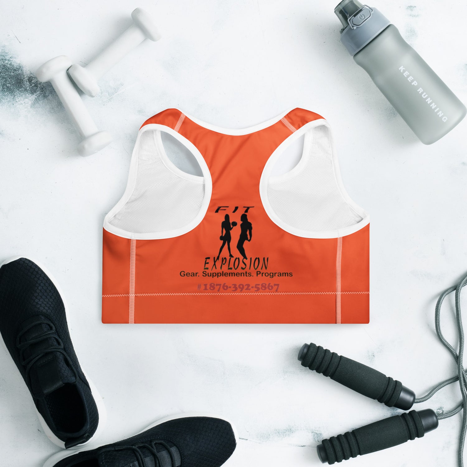 Orange sports bra with branding, black sneakers, gray water bottle, and jump rope on a white background