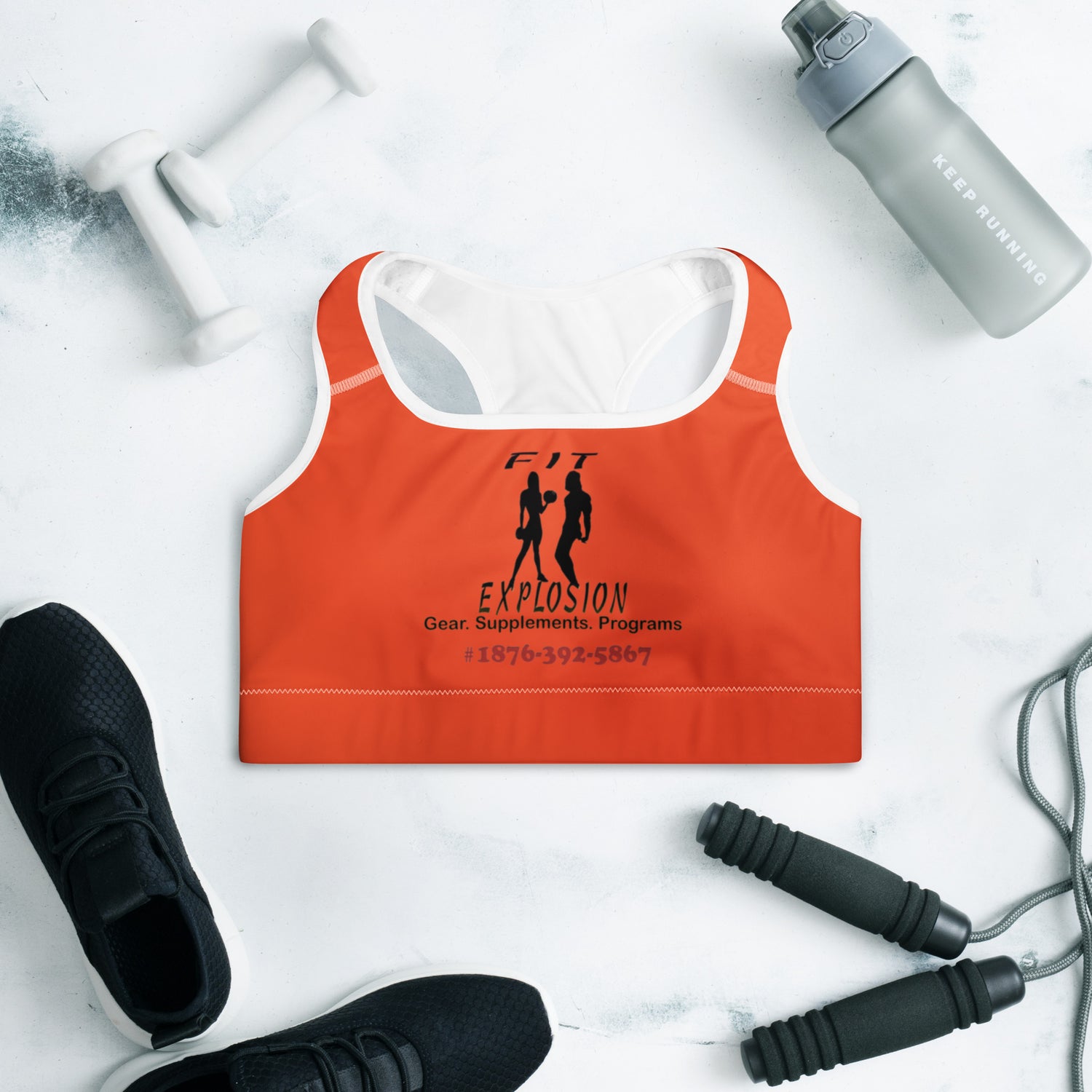 Orange sports bra with branding on a white surface with fitness equipment|IslandWear Fashion